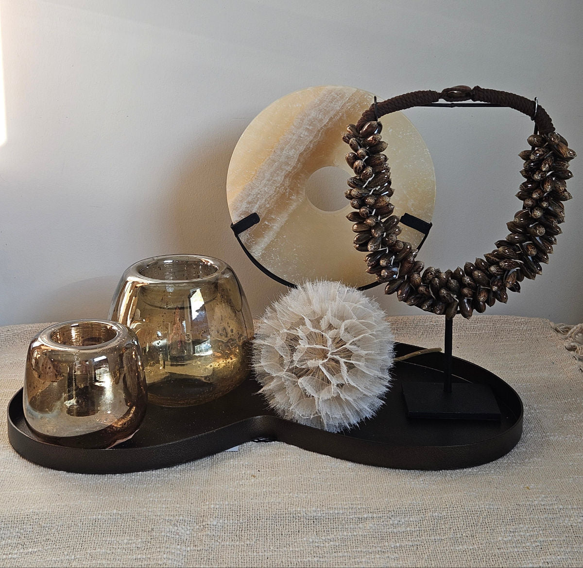 Sfeervol dienblad gedecoreerd met een schelpenketting, onyx steen ornament, s, twee glazen waxinelichthouders en een grote paardenbloem.
