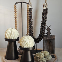  Woonaccessoires op een dienblad. Op het dienblad staat een schelpenketting, kralenketting, houten kam ornament, witte bloemen, twee kandelaren in verschillende hoogtes, met creme waxinelichthouders.