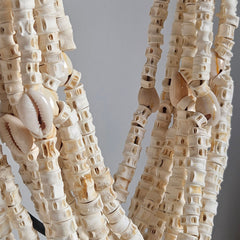 Close-Up van een witte schelpenketting. De kettings bestaat uit kleine ronde schelpjes aan een meerdere koorden.