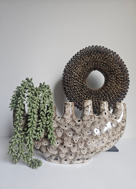 Vaas tulpenvaas speckled aardewerk gepresenteerd met een groene plant in een interieur met een schelpenketting