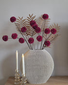 Vooraanzicht van burgundy-bruin Autumn Burgundy kunstboeket met stoffen bloemen in geribbelde vaas naast kaarsen