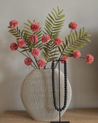 Vooraanzicht van roze-groen Meadow Blush kunstboeket met stoffen bloemen in geribbelde vaas naast zwarte kralen