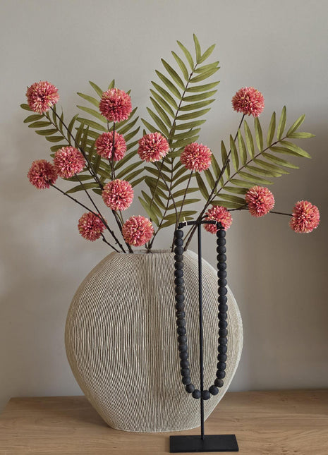 Vooraanzicht van roze-groen Meadow Blush kunstboeket met stoffen bloemen in geribbelde vaas naast zwarte kralen
