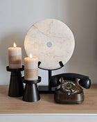 Interieurstyling op een dressoir: een rond wit ornament (Ø 30 cm), twee bruine kandelaren met LED-verlichting en een klassieke ouderwetse telefoon als blikvanger.