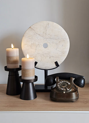 Interieurstyling op een dressoir: een rond wit ornament (Ø 30 cm), twee bruine kandelaren met LED-verlichting en een klassieke ouderwetse telefoon als blikvanger.