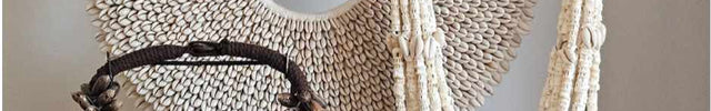 Woonaccessoires op een dressior met een schelpenkettingen in drie verschillende vormen. Grote rond vorm met witte schelpen, daarvoor twee kettingen in wit en en bruin. Ervoor staat een ouderwetse fotocamera. 
