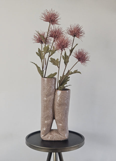 Vaas Looped roze beige aardewerk met lus-vorm en matte afwerking hoogte 31 cm getoond op een bijzettafel. De vaas heeft kleurrijke bloemen.