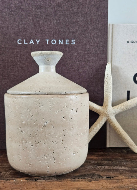 Beige potje met deksel  met deksel naast een witte zeester en woonboeken op een houten ondergrond
