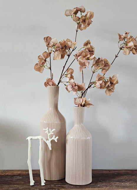 Twee geribbelde aardewerk vazen Conic in beige met droogbloemen naast een wit rendierornament op een houten ondergrond