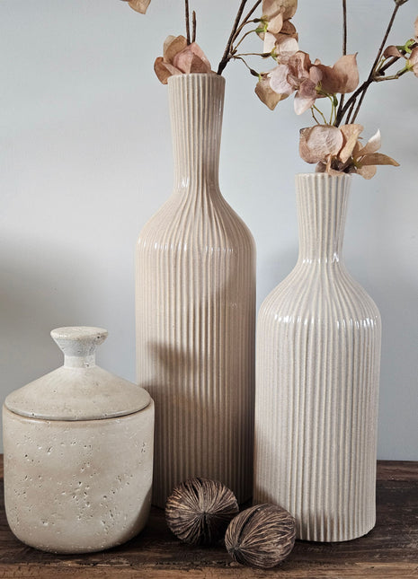 Twee geribbelde aardewerk vazen Conic in beige in formaat S en M met droogbloemen naast een wit rendierornament op een houten ondergrond