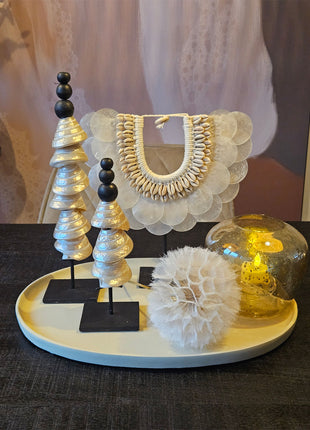 Dienblad Naomi taupe aluminium gepresenteerd op dressoir met schelpekettingen in het beige wit een waxinelichthouder in een bruine doorzichtekleur. gestyld met een grote paardebloem.