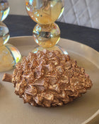 Dennenappel Catacol in crème-beige aardewerk met bruine accenten en een gekrulde steel op een dienblad met andere herfstdecoratie op een houten tafel