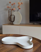 Dienblad Amy Ivory in druppelvorm van wit mat keramiek op een houten tafel naast twee amber glazen kandelaars met witte dinerkaarsen en een witte bolbloem