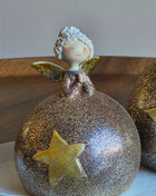 Close-up van engeltje S met witte krullende haren en gouden vleugels op een ronde glitterbol in goud-brons met een gouden ster op een wit oppervlak