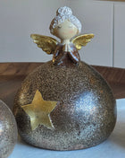 Close-up van engeltje M met witte krullende haren en gouden vleugels op een ronde glitterbol in goud-brons met een gouden ster op een houten ondergrond