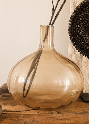 Glazen vaas bruin amber glanzend L met bolle ronde vorm en smalle hals op een houten dressoir met droge takken en een donkere schelpenketting op een standaard