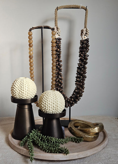 Dienblad met een schelpenketting en een kralenketting. Opgemaakt met een gouden ornament van twee schakels en robuuste bruine kandelaren. Het is een prachtige kant en klare set voor in huis.