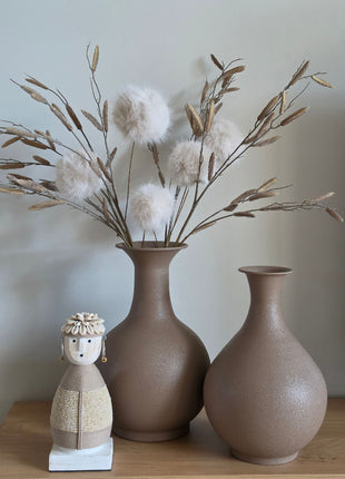 Vooraanzicht van twee taupe-bruine Faris metalen halsvazen met kunsttakken naast een beige Namji pop op hout
