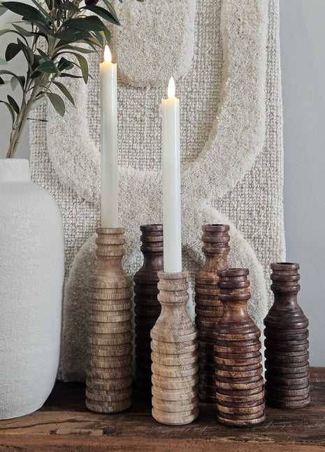 Set van vier houten kandelaars in lichtbruin en donkerbruin op een houten dressoir met een witte vaas en een decoratieve tak