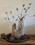 Vooraanzicht van twee beige Elora vazen met ruwe afwerking en kunstbloemen naast een glazen vaas op houten dienblad