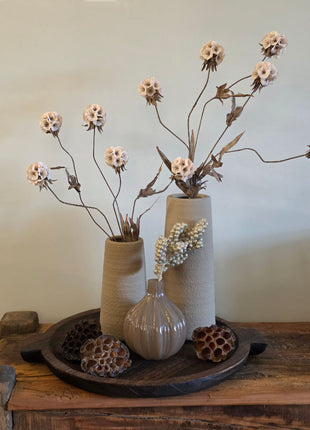 Vooraanzicht van twee beige Elora vazen met ruwe afwerking en kunstbloemen naast een glazen vaas op houten dienblad