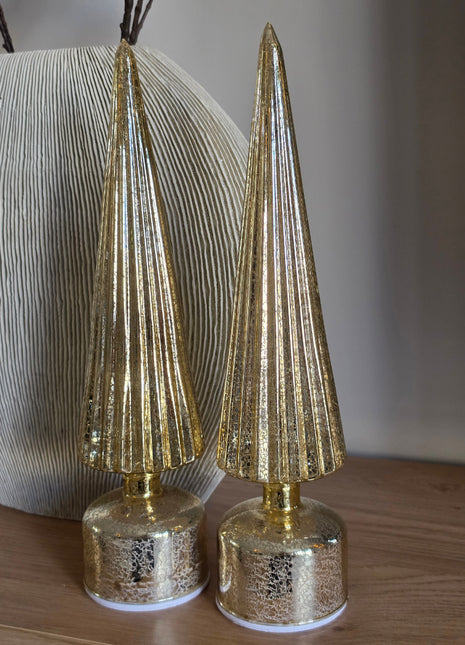 Set van twee kerstbomen LED van J-Line in goudkleurig geribbeld glas op ronde gouden voeten op een houten dressoir