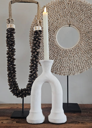 Kandelaar boog wit keramiek met een witte kaars op een houten dressoir naast een beige keramieke pot en een decoratieve tak