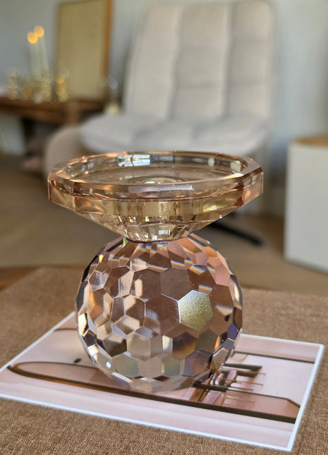 Kandelaar Lunelle M van Colmore in amber kristalglas met drie gestapelde gladde bollen op een donker houten tafel in een woonkamer met een witte bank