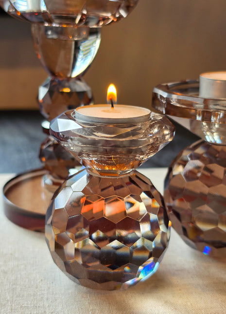 Kandelaar Lunelle S in amber kristalglas met twee gestapelde bollen en een komvormige houder met een brandend waxinelichtje op een donker houten oppervlak