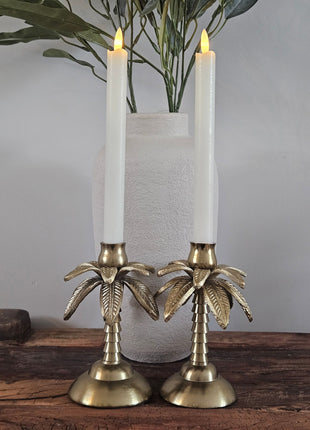 Kandelaar palmboom goud aluminium met een witte kaars naast een schelpenketting op een zwarte metalen standaard op een houten ondergrond