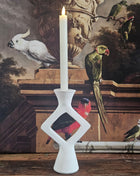 Kandelaar ruitvorm wit keramiek met een witte kaars op een houten dressoir naast een beige keramieke pot en een decoratieve tak