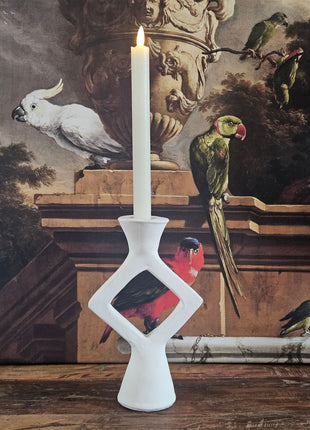 Kandelaar ruitvorm wit keramiek met een witte kaars op een houten dressoir naast een beige keramieke pot en een decoratieve tak
