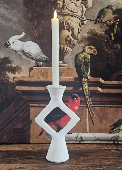 Kandelaar ruitvorm wit keramiek met een witte kaars op een houten dressoir naast een beige keramieke pot en een decoratieve tak