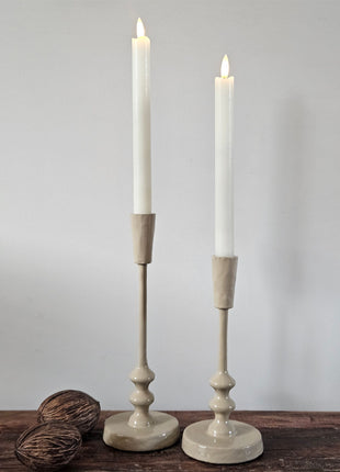 Set van twee geglazuurde ijzeren kandelaars Sand in zand-beige met witte diner LED-kaarsen naast drie droge noten op een houten ondergrond