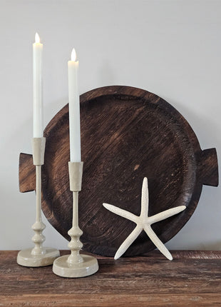 Twee geglazuurde ijzeren kandelaars Sand in zand-beige met witte diner LED-kaarsen naast een donker houten visschaal ornament en een witte zeester op een houten ondergrond