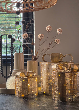 Vooraanzicht van goudkleurige kerstcadeautjes van metaaldraad met LED lichtjes naast kunstbloemen bij een raam