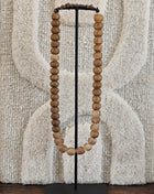 Kralenketting antique lichtbruin met ronde houten kralen op een zwart metalen standaard voor een geweven wandkleed