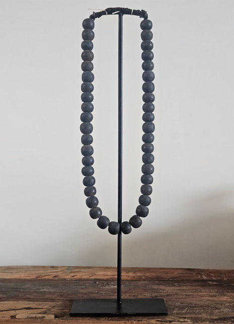 Kralenketting antique zwart met ronde donkergrijze kralen op een zwart metalen standaard op een houten ondergrond
