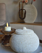 Kralenpotje Luna Wit met deksel volledig bedekt met kleine witte kraaltjes op een rond dienblad naast een brandende kaars op een amber glazen kandelaar en een geribbelde ronde vaas op een houten dressoir