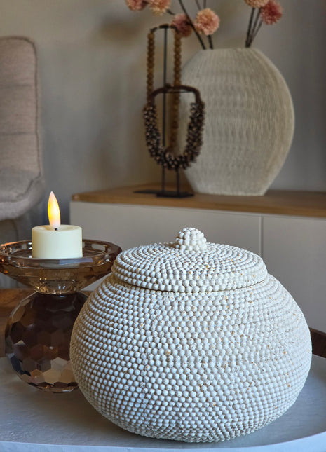Kralenpotje Luna Wit met deksel volledig bedekt met kleine witte kraaltjes op een rond dienblad naast een brandende kaars op een amber glazen kandelaar en een geribbelde ronde vaas op een houten dressoir