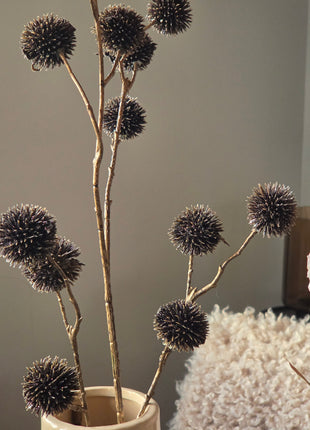 Vooraanzicht van bronskleurige Echinops kunsttakken met glanzende stekelige bollen in beige vaas naast pluizenbol