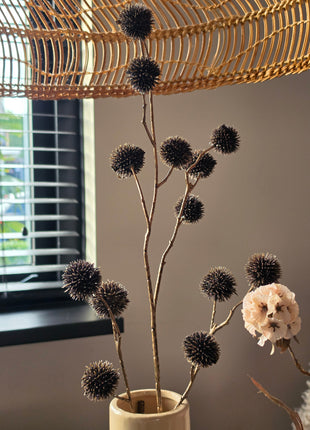 Vooraanzicht van bronskleurige Echinops kunsttakken met glanzende stekelige bollen in beige vaas onder rotan lamp