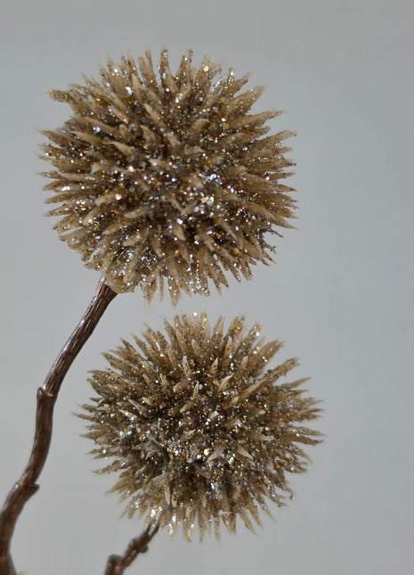 Close-up van champagnekleurige Echinops kunsttak met glitter op stekelige bollen tegen een grijze achtergrond