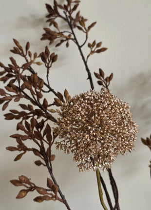 Close-up van goudkleurige Eupatorium kunsttak met glanzend bloemscherm naast bruine Wutong takken tegen grijs