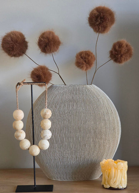 Vooraanzicht van bruine Fluffy Balls kunsttakken met pluizige vezelbollen in een geribbelde vaas naast kralen
