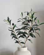 Kunsttak Olijftak Berry Spray - 70 cm op een creme kleurige vaas. De tak oogt realistisch en natuurlijk bijna niet van echt te onderscheiden.