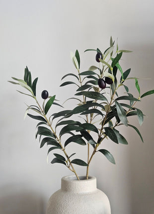 Kunsttak Olijftak Berry Spray - 70 cm op een creme kleurige vaas. De tak oogt realistisch en natuurlijk bijna niet van echt te onderscheiden.