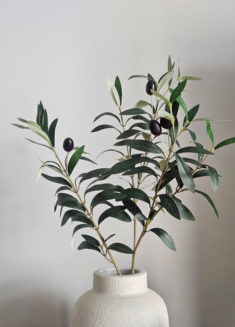 Kunsttak Olijftak Berry Spray - 70 cm op een creme kleurige vaas. De tak oogt realistisch en natuurlijk bijna niet van echt te onderscheiden.
