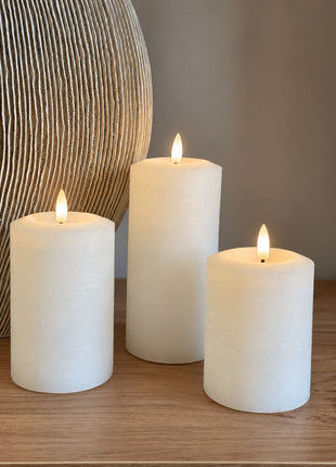 Vooraanzicht van drie cremewitte LED stompkaarsen van wax met verlichte vlammen naast een geribbelde vaas op hout