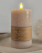 Jens Living LED stompkaars taupe op een keramieke schaal met een kraftpapieren band met opschrift LED Pillar Candle